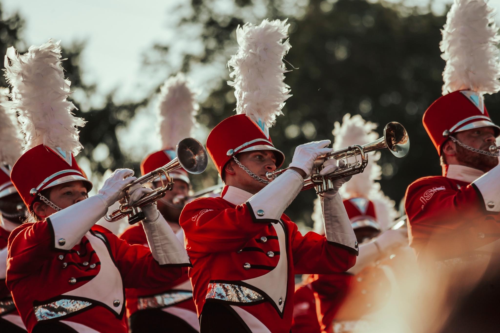 Marching band brass line in red uniforms with white plumes performing during a field show